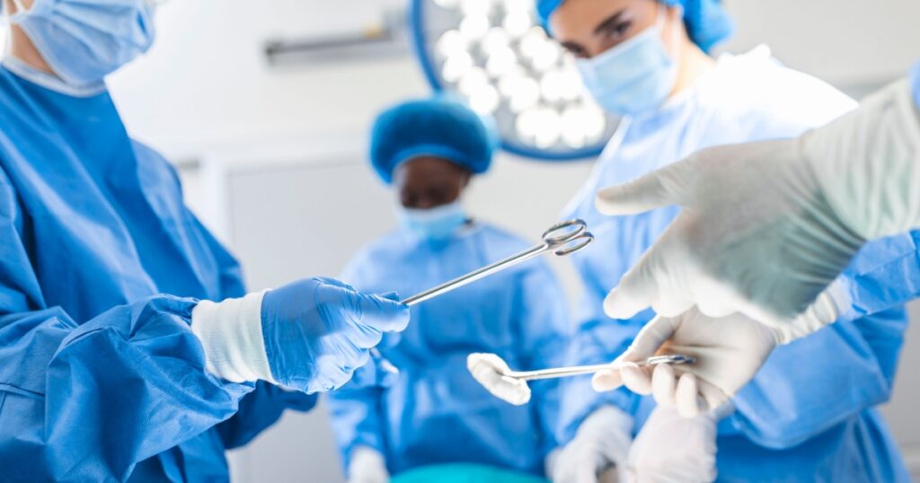 Low Angle Shot in the Operating Room, Assistant Hands out Instruments to Surgeons During Operation. Surgeons Perform Operation. Professional Medical Doctors Performing Surgery.