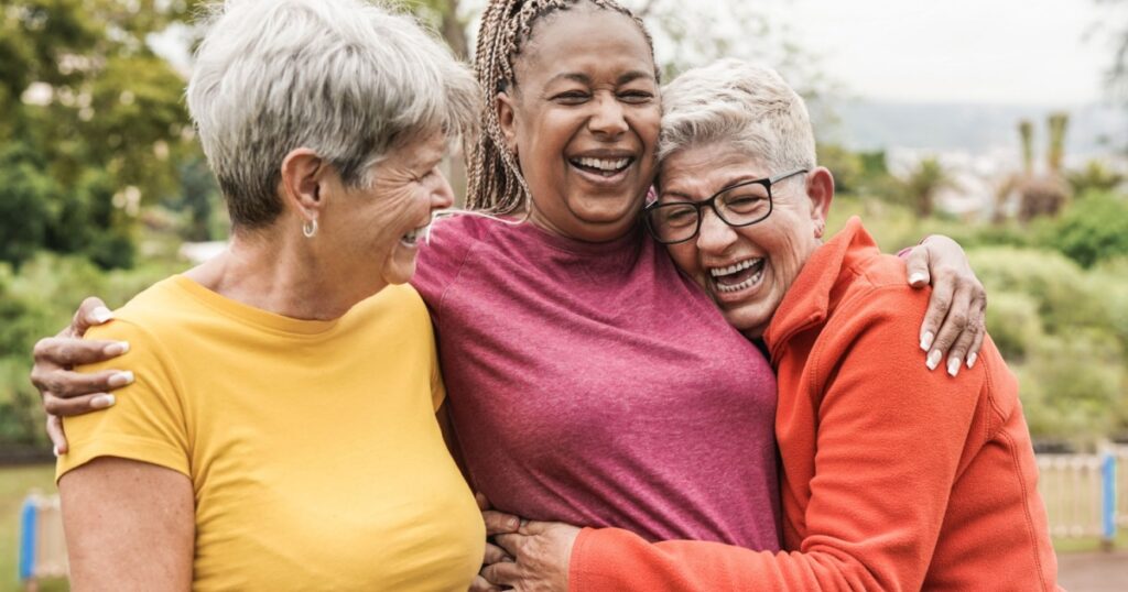 Happy multiracial senior women having fun together outdoor - Elderly generation people hugging each other at park