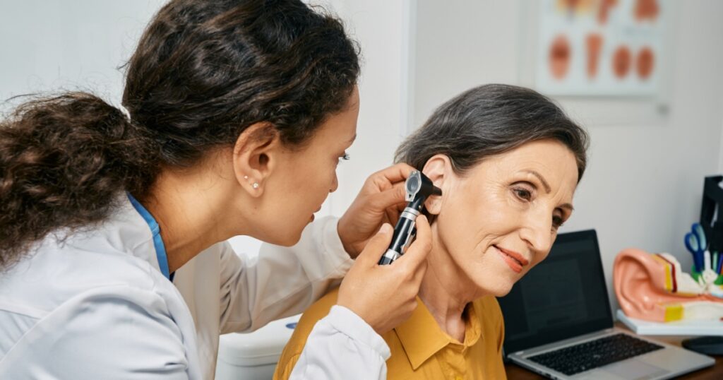 Hearing exam for elderly citizen people. Otolaryngologist doctor checking mature woman's ear using otoscope or auriscope at medical clinic