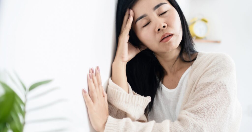 Asian woman having problem with Meniere's disease, fainting or dizziness hand holding her head leaning against the wall