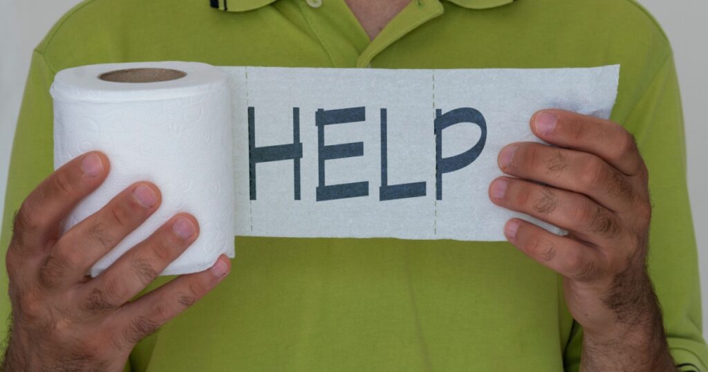 Help written on toilet paper roll in a man's hand. Concept of diarrhea and embarrassment.