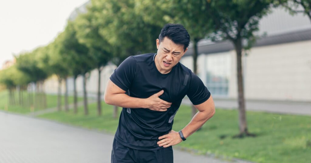 Male asian athlete, has chest pain fitness in the park and running, heart aches after cardio exercise