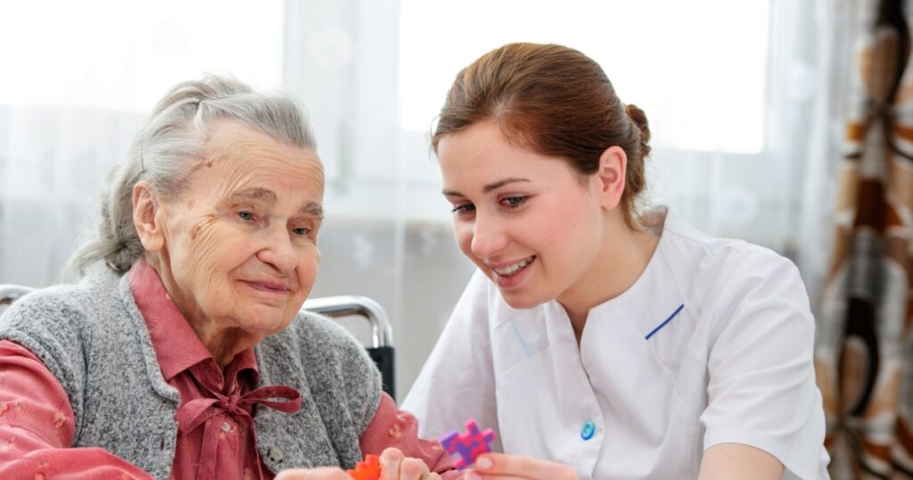 Elder care nurse playing jigsaw puzzle with senior woman in nursing home