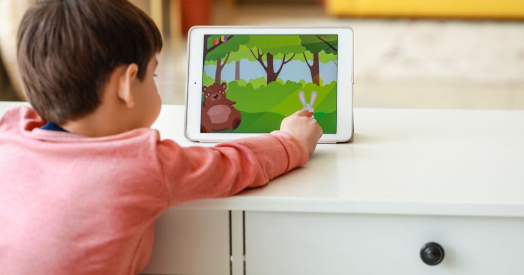 Little boy watching cartoons on tablet computer at table in living room