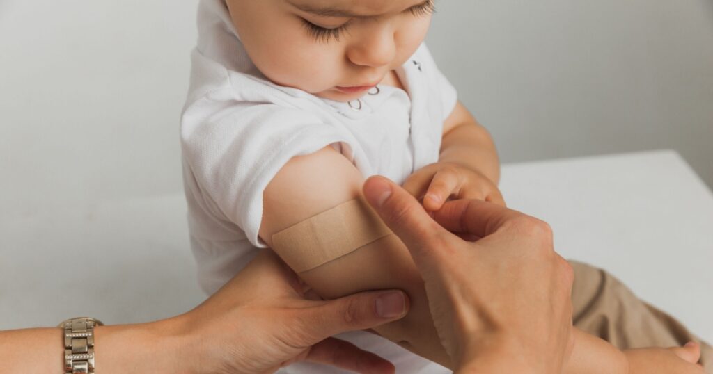 The doctor puts a patch on the child's shoulder after injecting the vaccine with a syringe. The patient receives first aid. Close-up. Vaccination for children.