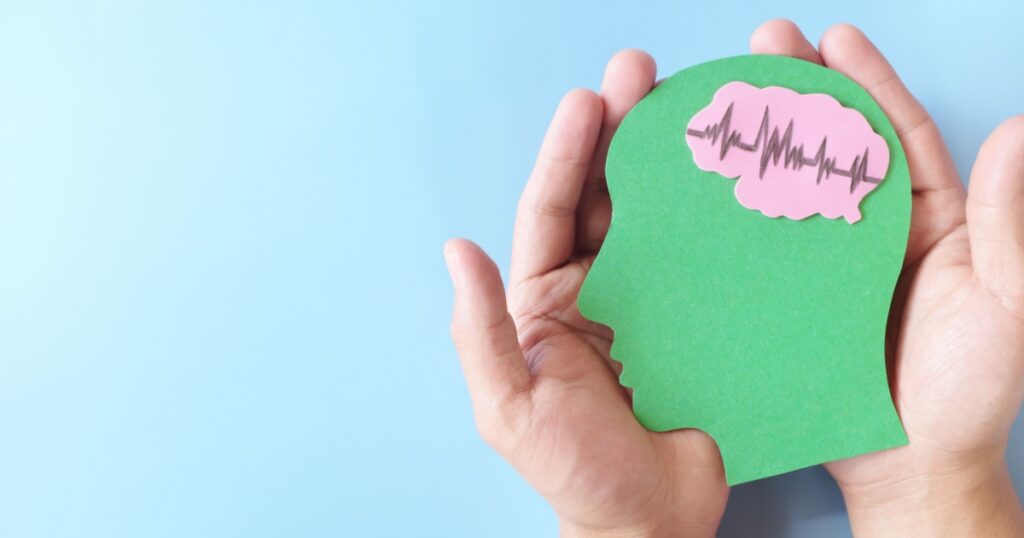 Hand holding human head profile cutout with healthy brain. Care for good memory, ADHD, Alzheimer, stroke, dementia prevention and world mental health day awareness concept.