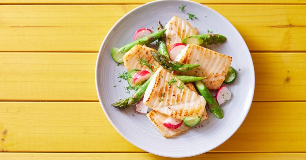 Top view of palatable grilled tilapia fish with cut vegetables served on plate on wooden table