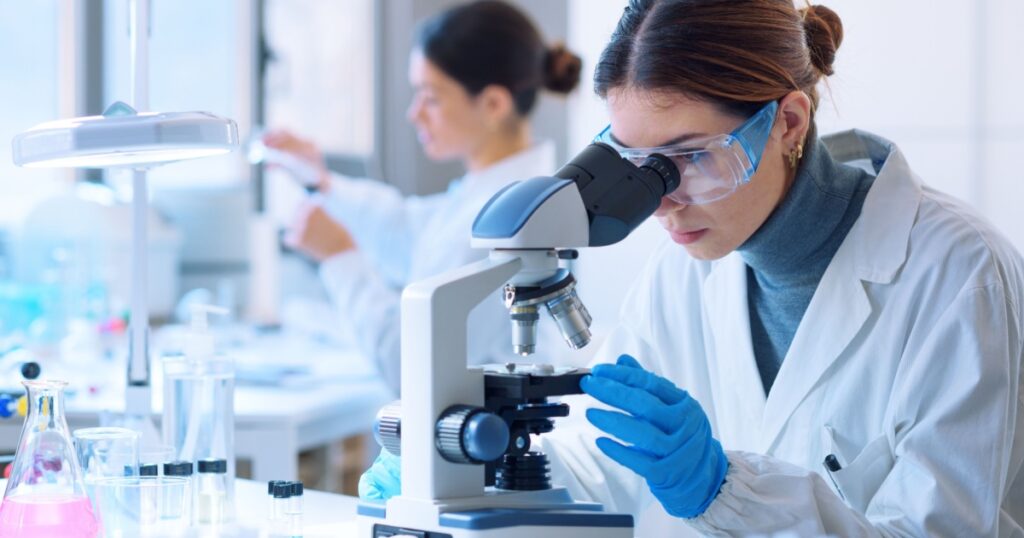 Young scientists conducting research investigations in a medical laboratory, a researcher in the foreground is using a microscope