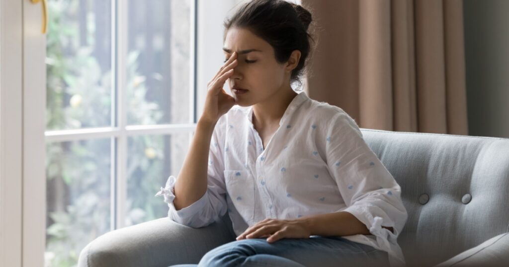 Depressed frustrated young Indian woman suffering from headache, migraine, touching face, head with closed eyes, feeling stressed, sick, tired, thinking over bad news, problems, crisis