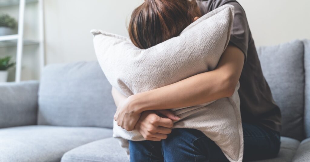 Unhappy anxiety young Asian woman covering her face with pillow on the cough in the living room at home.