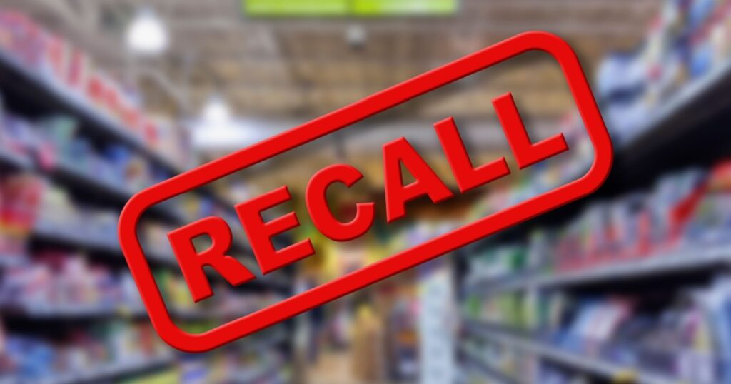 Blurry interior of a grocery store aisle behind large red Recall text