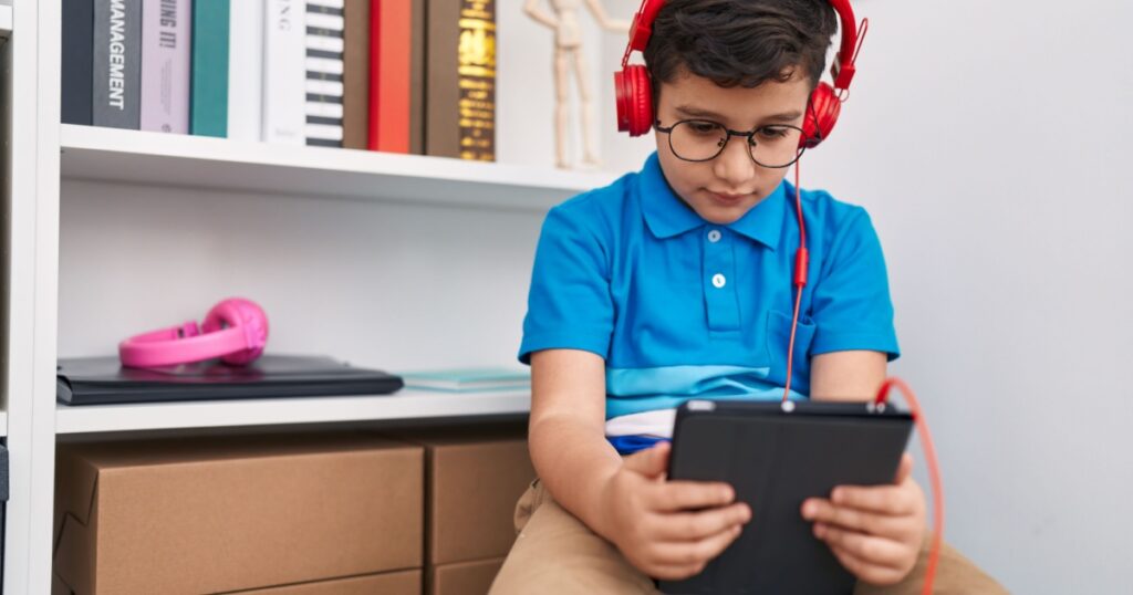 Adorable hispanic boy student watching video on touchpad at library school