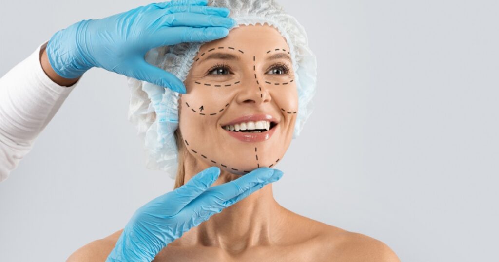 Cheerful excited middle aged woman in medical hat with pre surgery marks on her face looking at copy space for ad and smiling, surgeon hands in blue gloves touching female skin