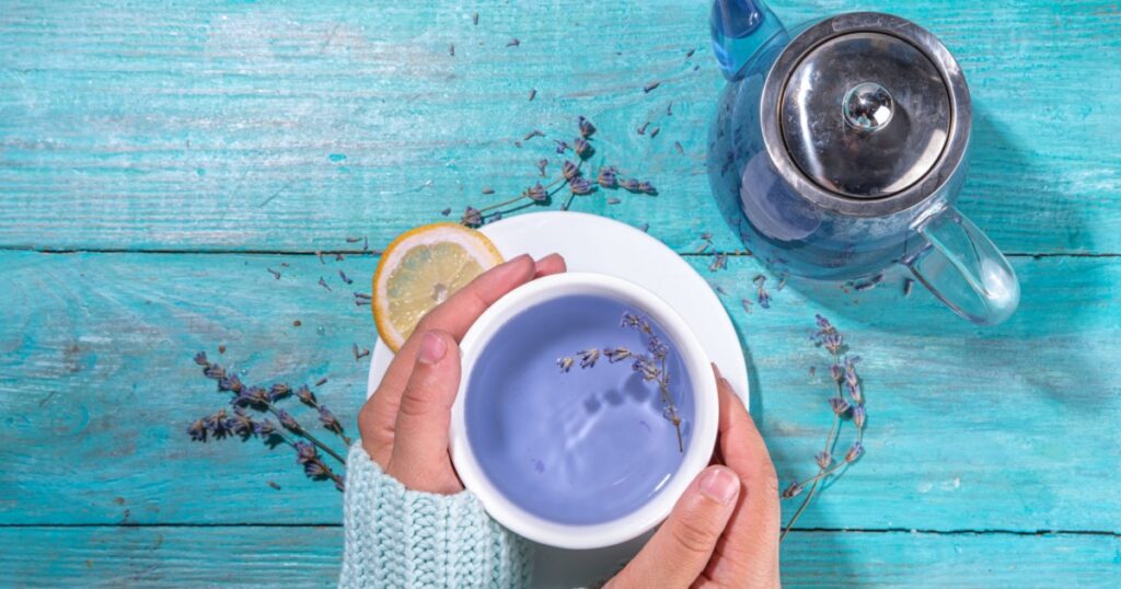 Cup of aromatic lavender tea with a pile of lavandula flowers, lemon and honey, top view on blue wood table copy space