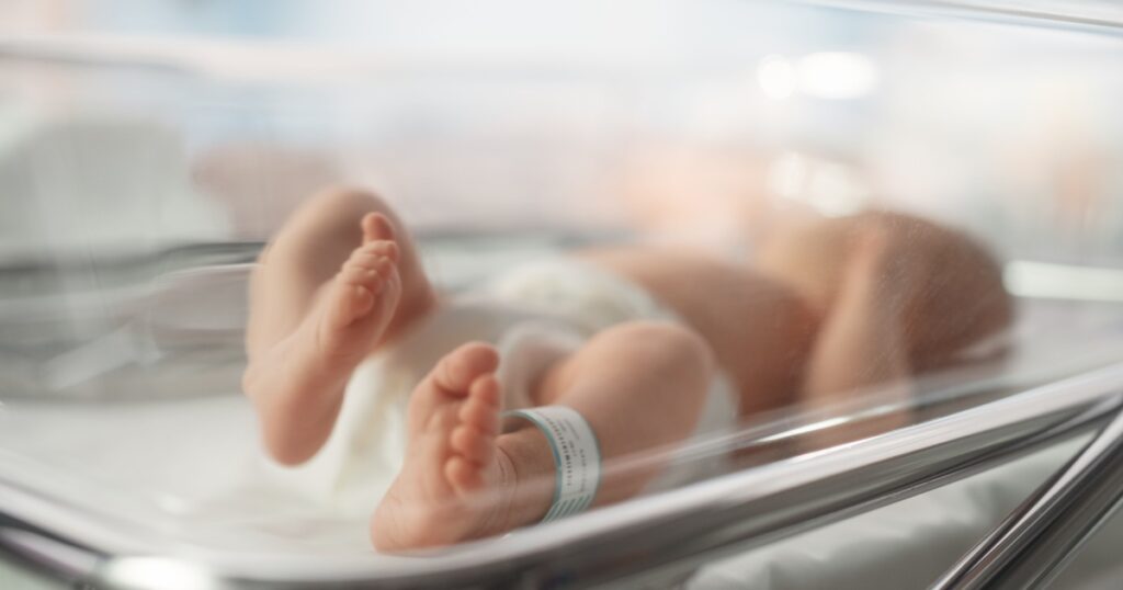 Cute Little Caucasian Newborn Baby Lying in Bassinet in a Maternity Hospital. Portrait of a Tiny Playful and Energetic Child with a Name ID Tag on the Leg. Healthcare, Pregnancy and Motherhood Concept
