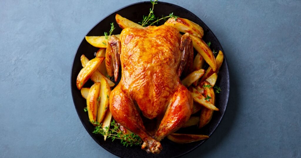 Roasted chicken with potatoes on dark plate. Grey background. Close up. Top view.
