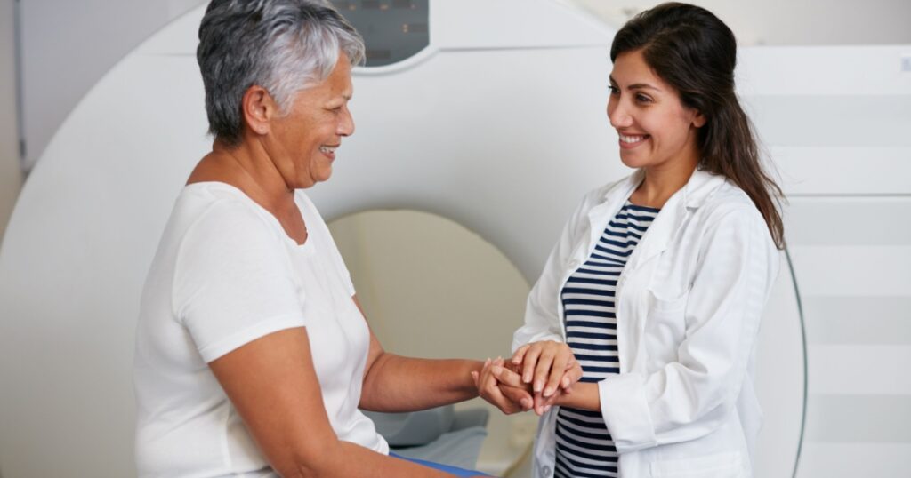 Doctor, ct scan and woman holding hands of patient in hospital before scanning in machine. Mri, comfort and happy medical professional with senior female person before radiology test for healthcare.