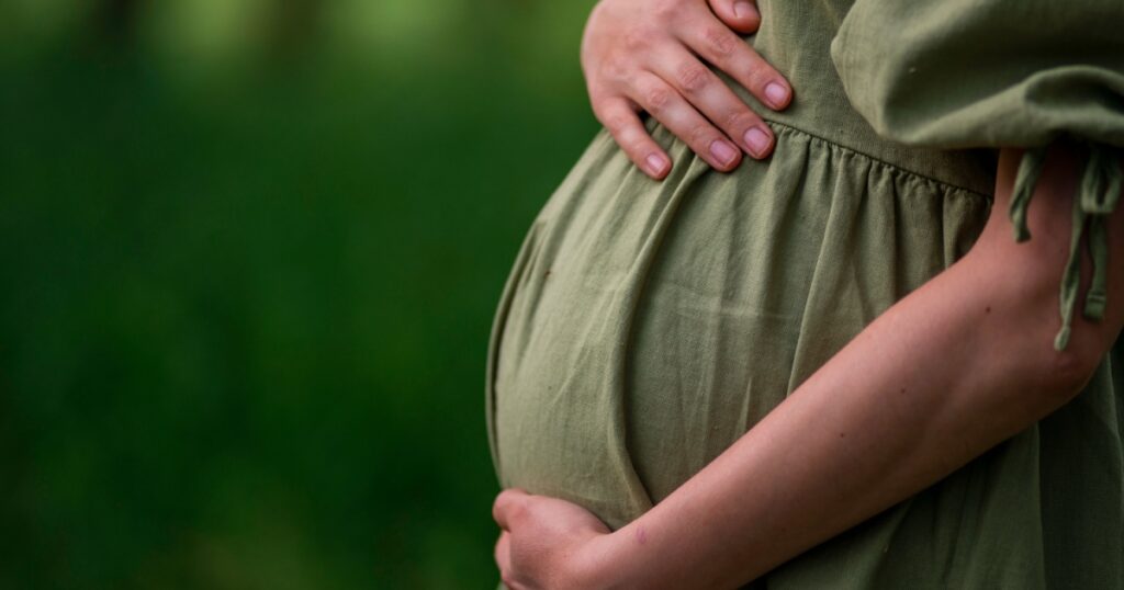 Caucasian Young Pregnant woman Tummy belly summer green dress touching stomach field expecting a baby relaxing outside nature park lake rural Beautiful magic 8 months enjoying life glasses hat