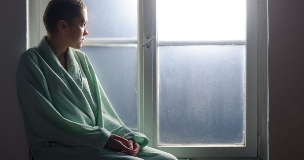 Young cancer patient sitting in front of hospital window.