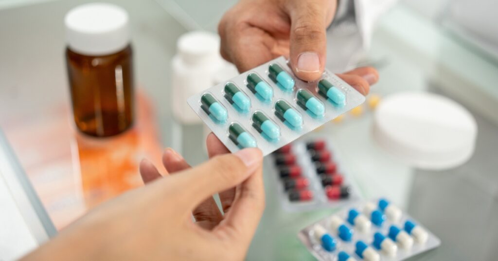 Pharmacist recommends medicines to customers. Asking the questions of medication. Professional Asian male pharmacist giving prescription medications to female patient customers at drugstore shelves.