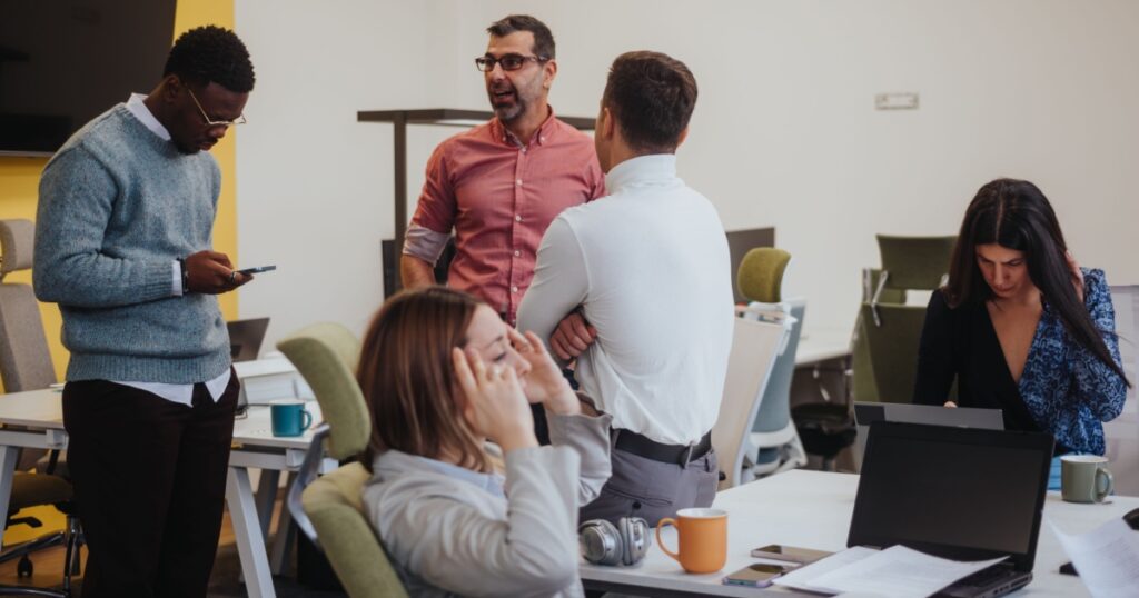 Young, female employee struggling severe headaches caused of migraine during working hours with her coworkers at modern office.