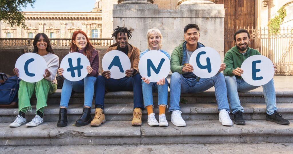 Group of diverse young students holding letters spelling 'CHANGE', advocating for social causes on campus steps.