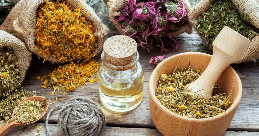 Healing herbs in hessian bags, mortar with chamomile and essential oil on wooden table, herbal medicine.