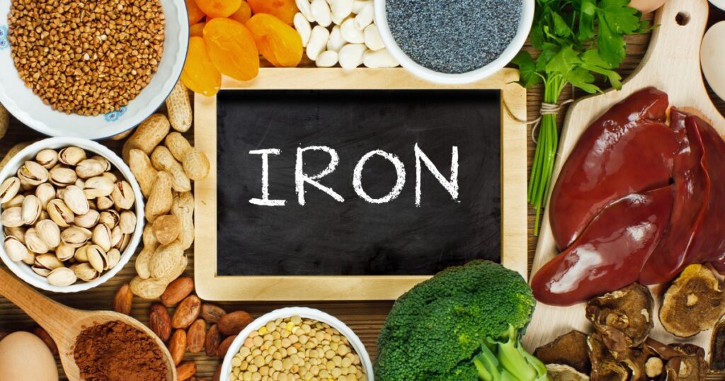 Collection iron rich foods as liver, buckwheat, eggs, parsley leaves, dried apricots, cocoa, lentil, bean, blue poppy seed, broccoli, dried mushrooms, peanuts and pistachios on wooden table.