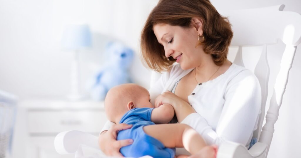 Young mother holding her newborn child. Mom nursing baby. Woman and new born boy in white bedroom with rocking chair and blue crib. Nursery interior. Mother playing with laughing kid. Family at home