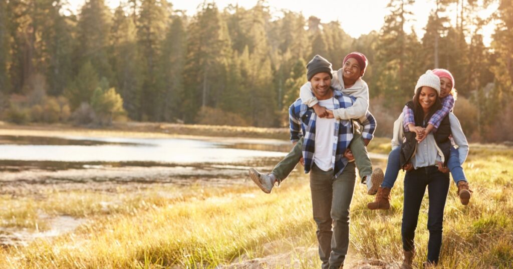 Parents Giving Children Piggyback Ride On Walk By Lake
