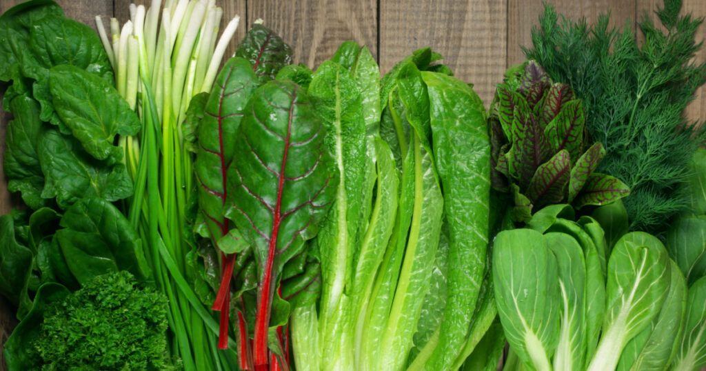 Spring vitamin set of various green leafy vegetables on rustic wooden table. Top view point.