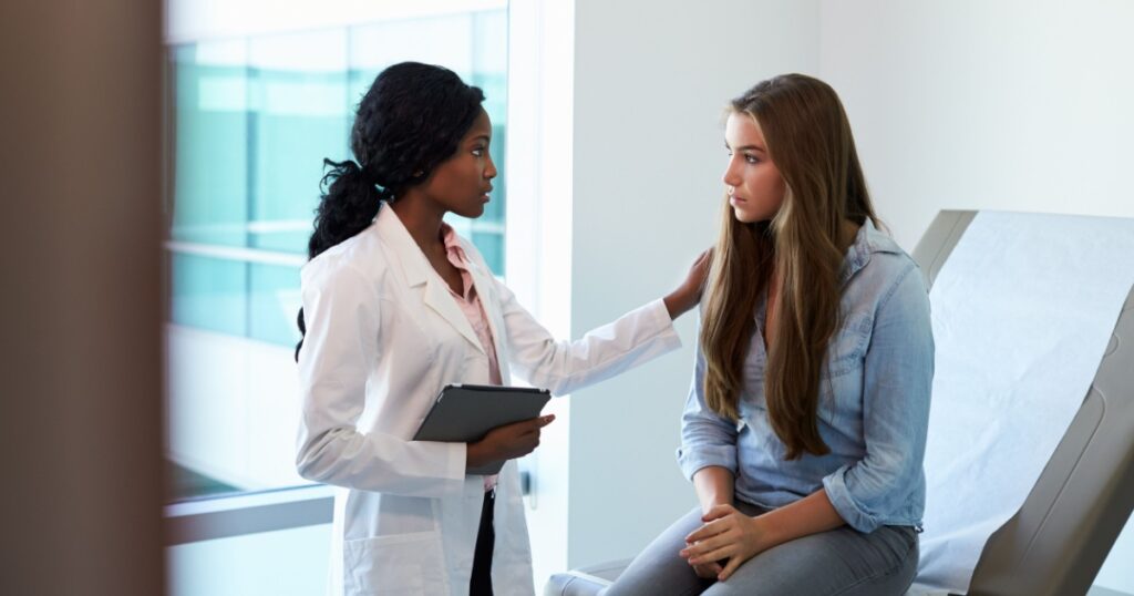 Doctor Talking To Unhappy Teenage Patient In Exam Room