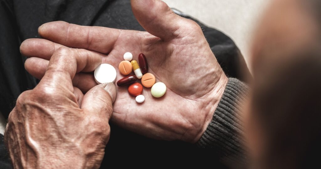 Many multi-colored pills in a Senior's hands. Painful old age. Caring for the health of the elderly
