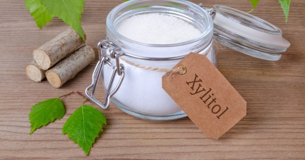 sugar substitute xylitol, a glass jar with birch sugar, liefs and wood on wooden background