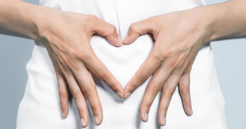 young woman who makes a heart shape by hands on her stomach.