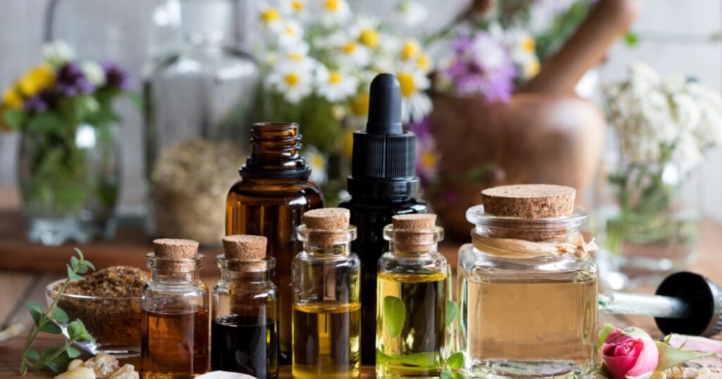 Selection of essential oils with various herbs and flowers in the background