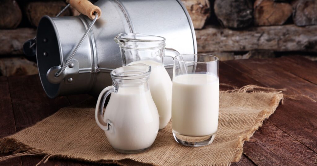 A jug of milk and glass of milk on a wooden table