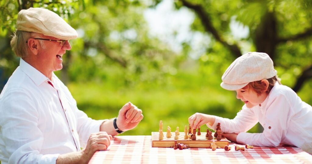 happy grandpa and grandson playing chess in spring garden