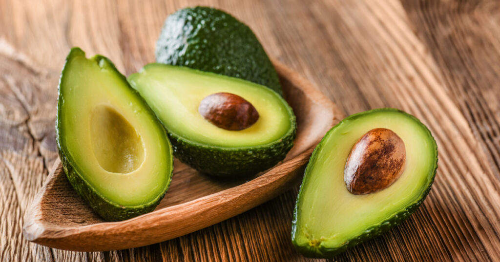 Avocado on old wooden table.Halfs on wooden bowl. Fruits healthy food concept.