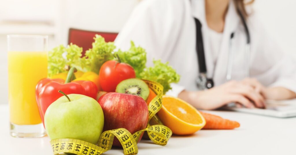 Nutritionist desk with healthy fruit, juice and measuring tape. Dietitian working on diet plan. Weight loss and right nutrition concept
