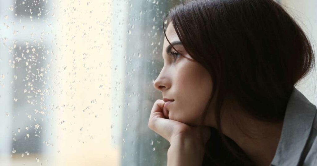 woman with melancholy stare looking out a window. Depression and mood disorder concept