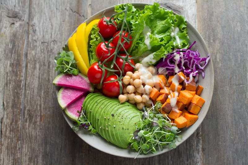 colorful vegan salad with avocado, chickpeas, yellow peppers, cherry tomatoes on the vine, cubed sweet potato, clover sprouts, lettuce, and purple cabbage. 