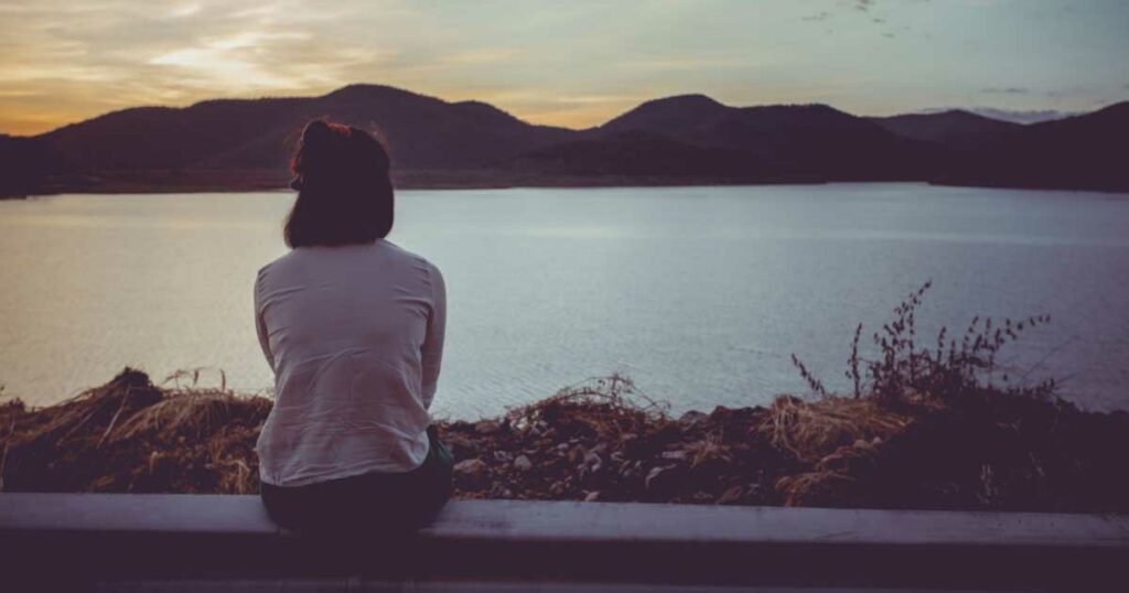 Woman sitting looking at view of river and mountains 