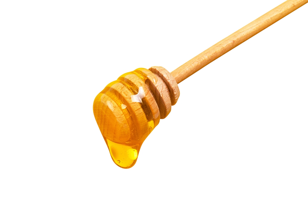 Honey dripping from honey dipper isolated on white background. Thick honey dipping from the wooden honey spoon. Healthy food and diet concept
