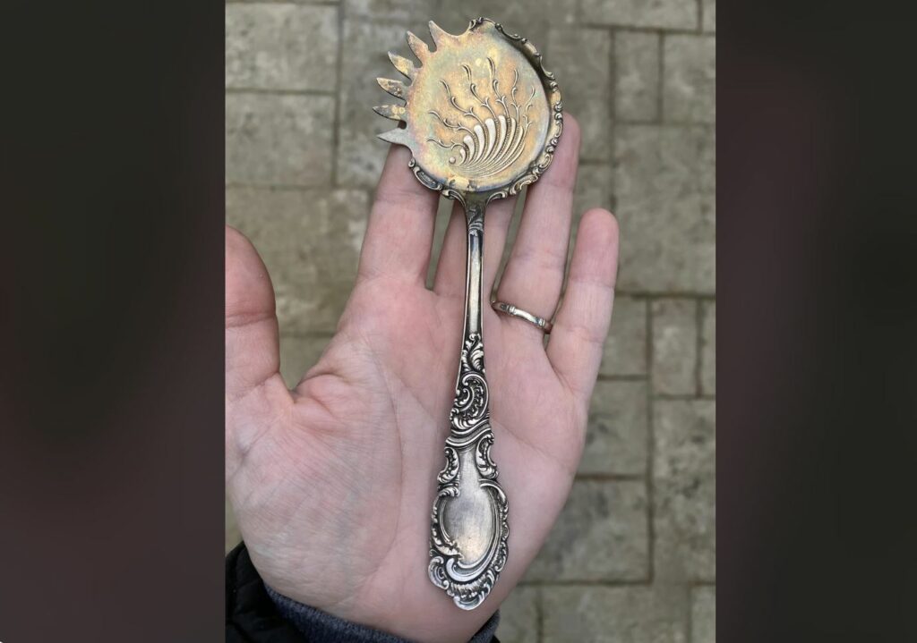 Hand holding strange object that appears to be a spoon. Stone rectangles in the background.