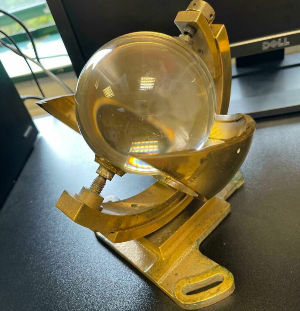 Glass sphere between metal with a computer monitor and a window in the background.