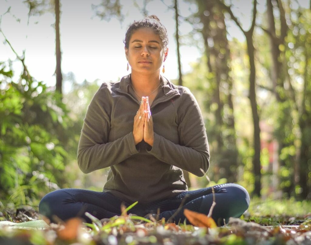 Woman meditating in the woods. Blurred trees and foliage in the background.