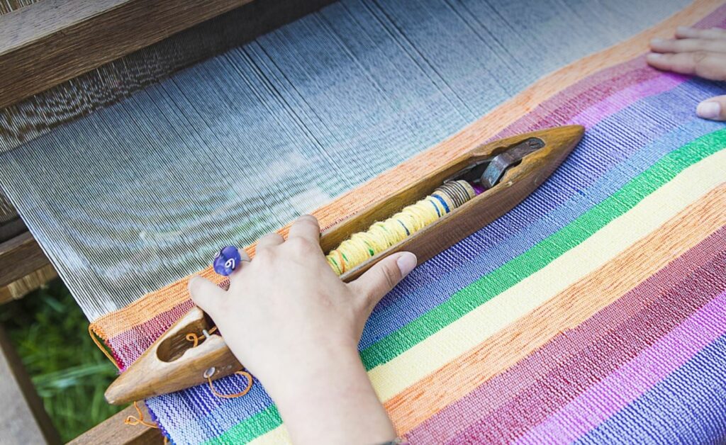Hands weaving rainbow fabric.