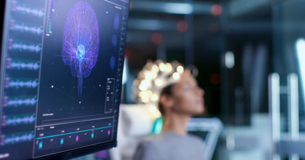 Woman Wearing Brainwave Scanning Headset Sits in a Chair In the Modern Brain Study Laboratory/ Neurological Research Center. Monitors Show EEG Reading and Brain Model.