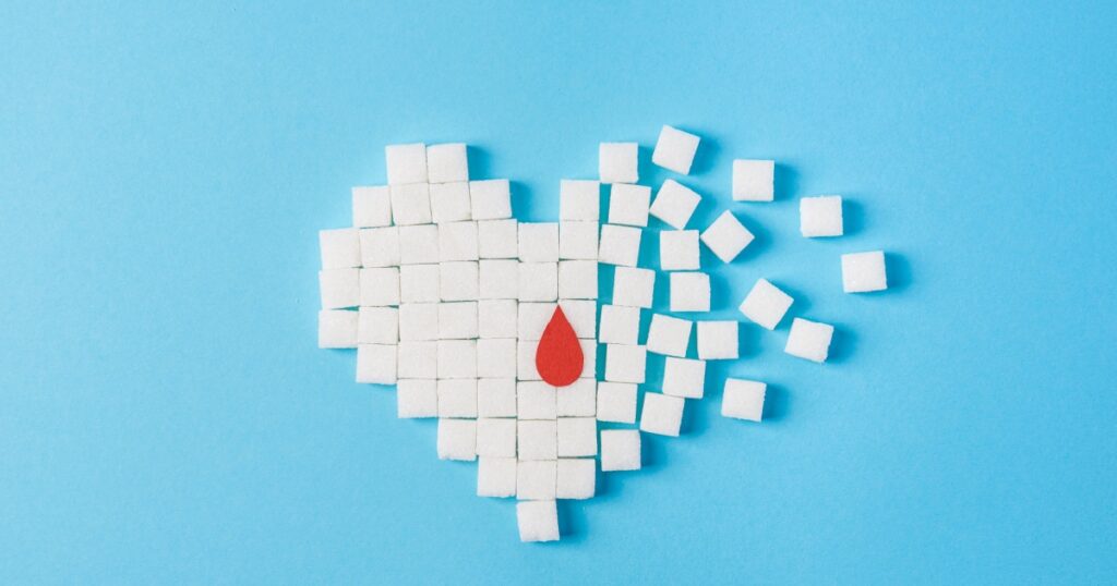 the drop of blood on broken heart made of pure white cubes of sugar isolated on blue background, World diabetes day, November 14